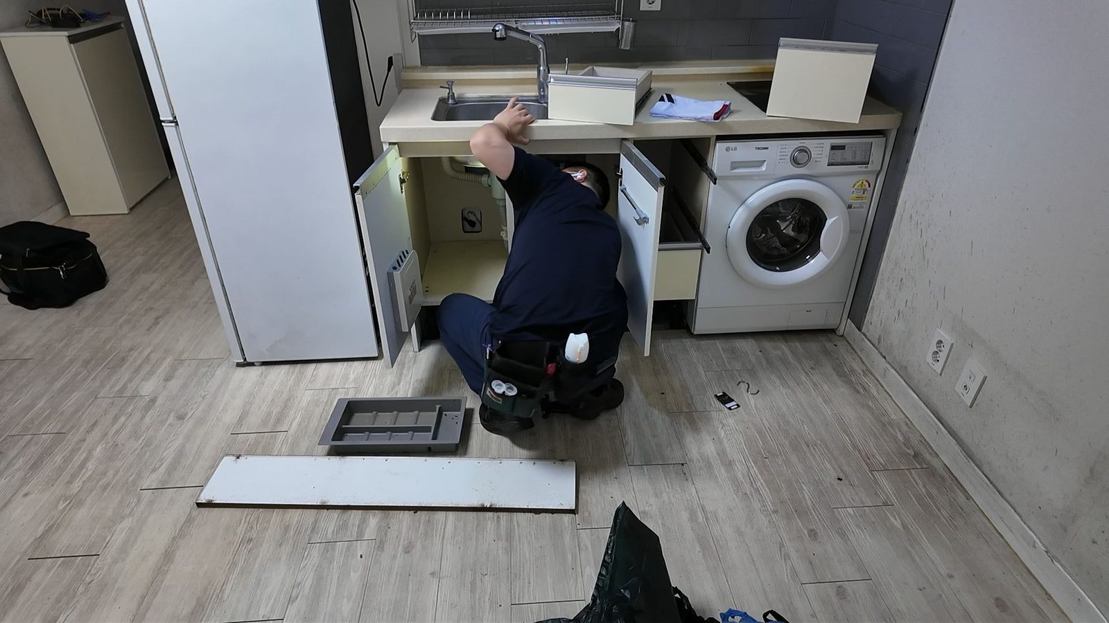 싱크대 하부장 문과 서랍을 모두 분리해 배관 주변까지 드러낸 상태로 작업하는 모습